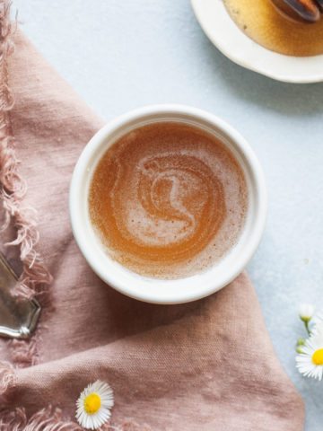 a small bowl of honey syrup with a pink napkin, flowers, and honey wand