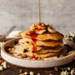 plate of banana pancakes being drizzled with syrup