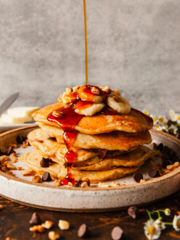 plate of banana pancakes being drizzled with syrup