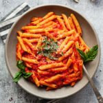 a plate of penne al pomodoro with basil and a fork