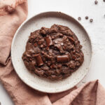 a single serve vegan chocolate brownie cookie on a plate with a pink napkin