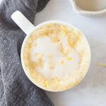 a glazed lemon mug cake in a white mug on a marble table