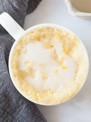 a glazed lemon mug cake in a white mug on a marble table