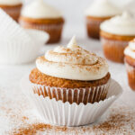 an applesauce cupcake topped with cream cheese frosting and cinnamon with more cupcakes in the background
