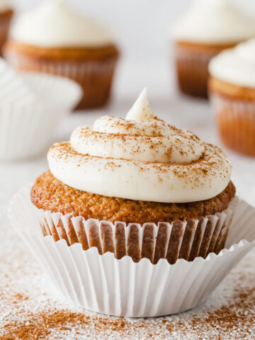 an applesauce cupcake topped with cream cheese frosting and cinnamon with more cupcakes in the background