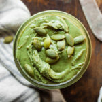 green pumpkin seed butter in a jar topped with pumpkin seeds