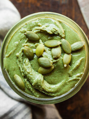 green pumpkin seed butter in a jar topped with pumpkin seeds