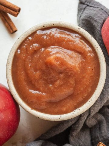 ramekin full of apple butter surrounded by apples and cinnamon sticks