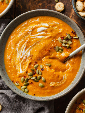 a bowl of vegan pumpkin soup topped with pumpkin seeds with a spoon in it