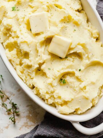 a dish of mashed potatoes made without milk topped with pats of butter and herbs.