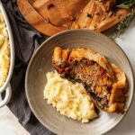 A slice of veggie wellington on a plate next to mashed potatoes.