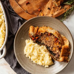A slice of veggie wellington on a plate next to mashed potatoes.