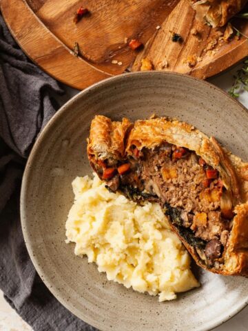 A slice of veggie wellington on a plate next to mashed potatoes.