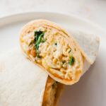breakfast burrito cut in half showing inside stuffed with eggs, spinach, and cheese