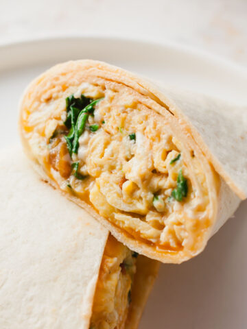 breakfast burrito cut in half showing inside stuffed with eggs, spinach, and cheese