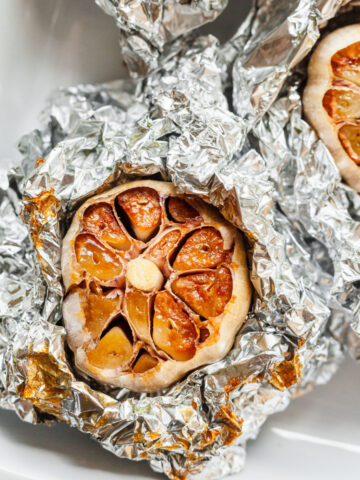 a close up of roasted garlic wrapped in foil in a baking dish