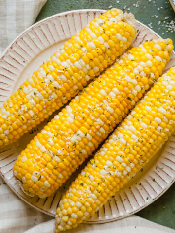 three ears of baked corn on the cob on a white plate topped with salt
