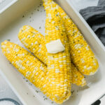 ears of corn in a white baking dish topped with a pat of butter