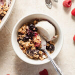 a bowl of mixed berry crisp topped with vanilla ice cream with a spoon sticking out of it