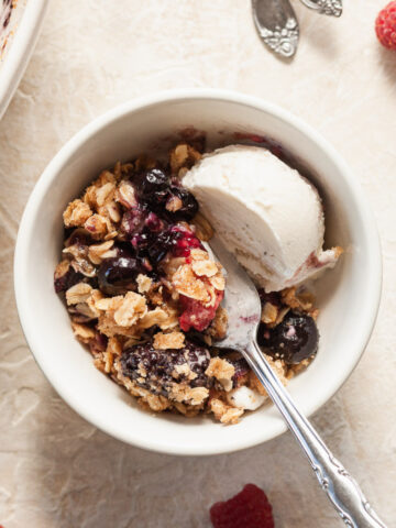 a bowl of mixed berry crisp topped with vanilla ice cream with a spoon sticking out of it