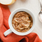 Top down view of apple mug cake next to a red napkin, a spoon, and an apple.