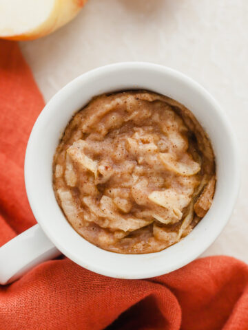 Top down view of apple mug cake next to a red napkin, a spoon, and an apple.