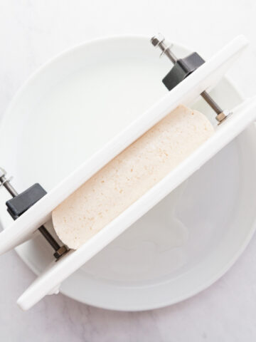 Tofu in a tofu press in a shallow bowl.
