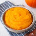 Pumpkin puree in a bowl on top of a blue striped napkin with a wooden spoon next to it.