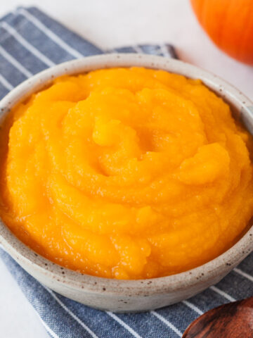 Pumpkin puree in a bowl on top of a blue striped napkin with a wooden spoon next to it.