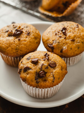 Three Mini Pumpkin Chocolate Chip Muffins on a round white plate.