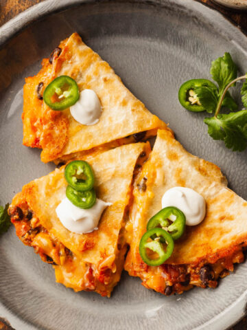 Black Bean and Butternut Squash Quesadillas on a plate topped with jalapenos and sour cream.