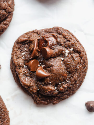 Whole wheat chocolate fudge cookies on parchment paper next to chocolate chips.
