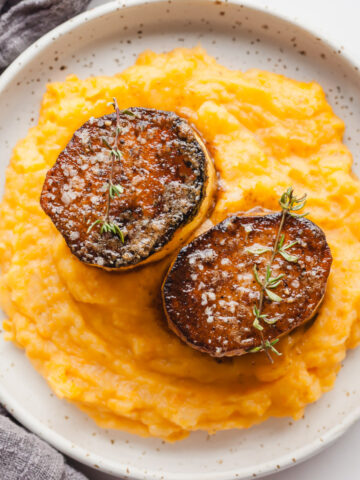 Two fondant potatoes on a bed of sweet potato mash on a white plate next to a gray napkin.