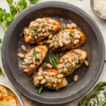 White bean crostini on a gray plate topped with fresh rosemary and parmesan cheese, next to a bunch of parsley and a sprig of rosemary.