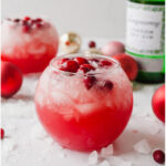 Christmas gin cocktail in a round glass surrounded by ice cubes and frozen cranberries.