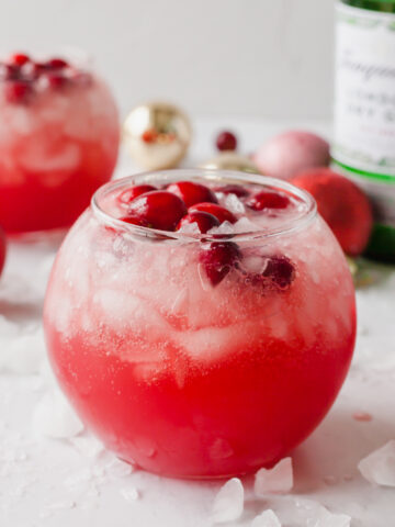 Christmas gin cocktail in a round glass surrounded by ice cubes and frozen cranberries.