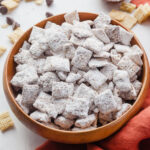Puppy chow in a wooden bowl surrounded by rice chex and chocolate chips.