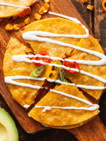 Top view of a Corn and Sweet Pepper Quesadillas topped with slices of mini bell peppers and sour cream on a wooden cutting board.