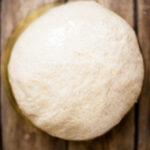 a ball of pizza dough in a glass bowl on a wood table