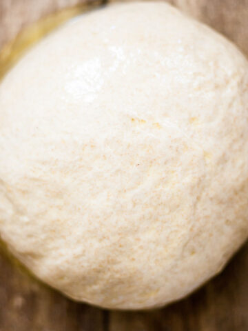 a ball of pizza dough in a glass bowl on a wood table