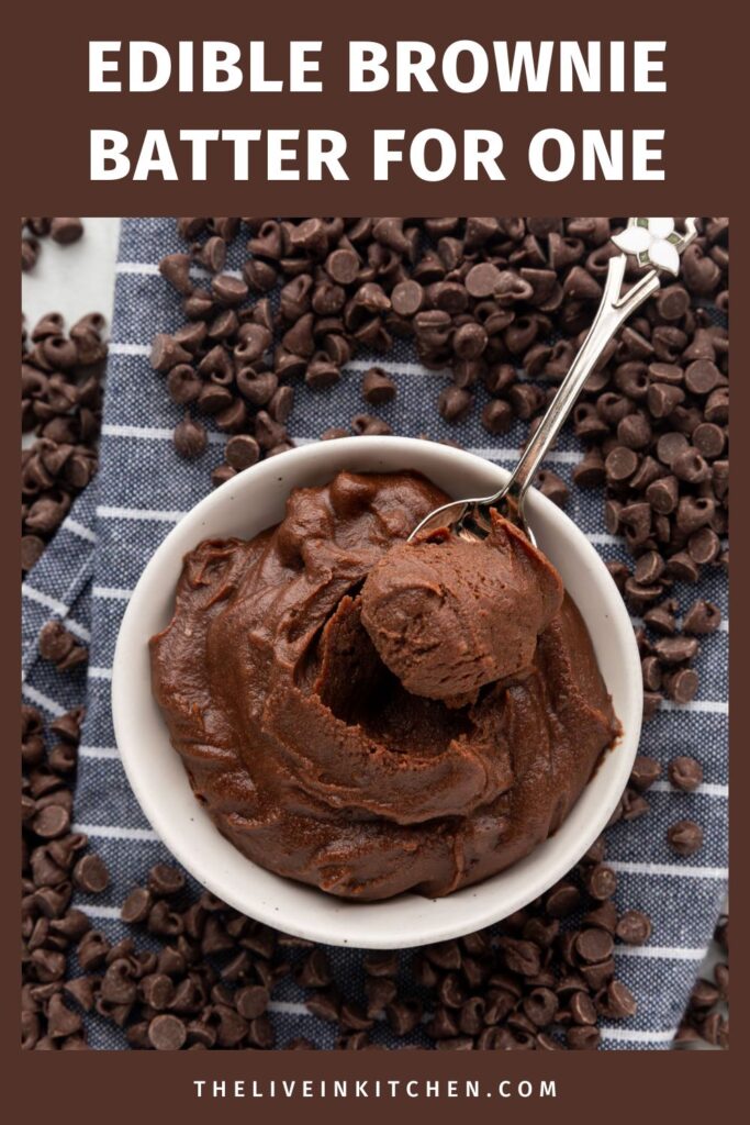 Edible brownie batter with a spoon sticking out of it on a blue and white striped napkin surrounded by chocolate chips.