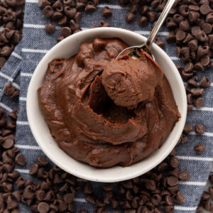Edible brownie batter with a spoon sticking out of it on a blue and white striped napkin surrounded by chocolate chips.