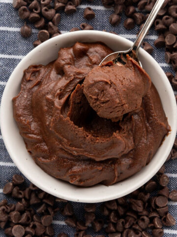 Edible brownie batter with a spoon sticking out of it on a blue and white striped napkin surrounded by chocolate chips.