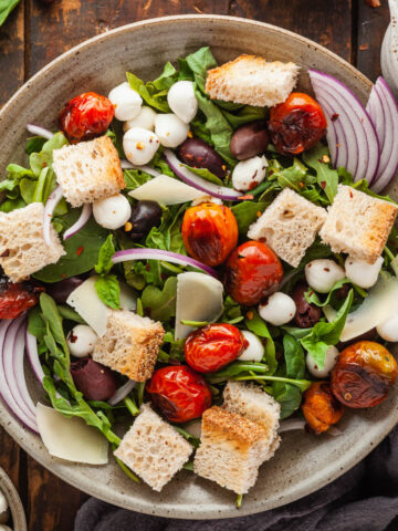 A bowl of pizza salad next to a cup of dressing.