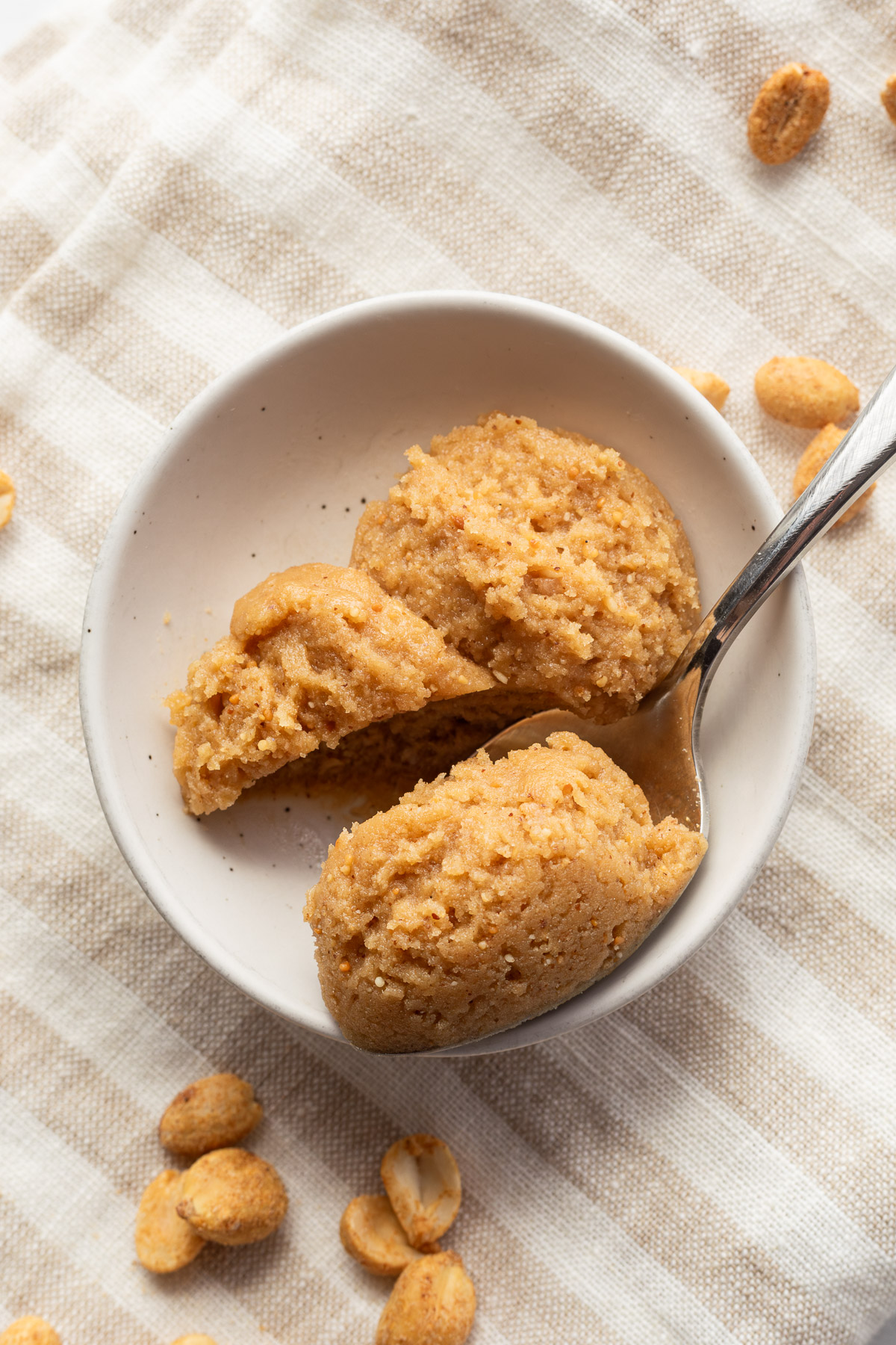 Two scoops of edible peanut butter cookie dough in a small white bowl with a spoon taking a bite.