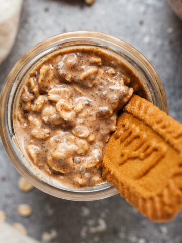 A jar of biscoff overnight oats with a lotus cookie sticking out of it.