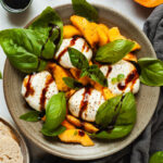 Peach burrata caprese in a shallow bowl drizzled with balsamic glaze.