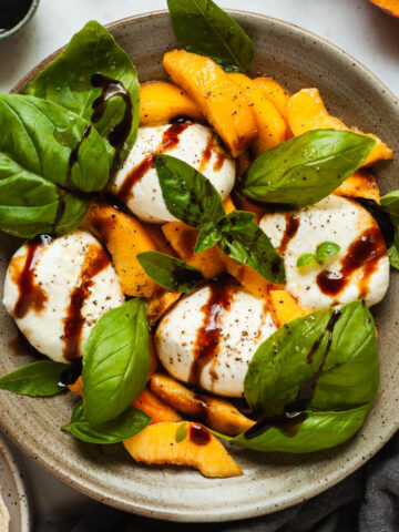 Peach burrata caprese in a shallow bowl drizzled with balsamic glaze.