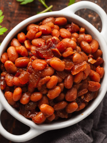 A small white bowl with handles filled with vegetarian baked beans.