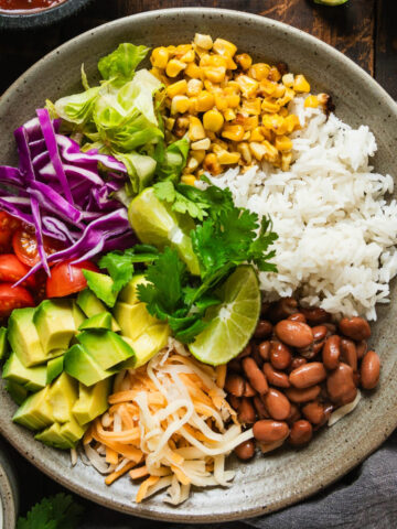 A burrito bowl full of rice, vegetables, cheese, and pinto beans.